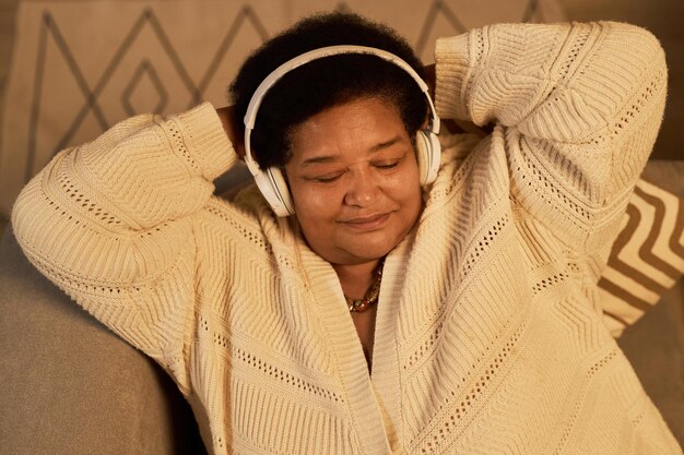 A person wearing headphones, eyes closed, with a serene expression, listening to ASMR content on their laptop. The room is dimly lit, creating a cozy and relaxing atmosphere. Soft focus on the face to emphasize relaxation.